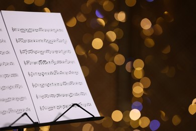 Photo of Note stand with music sheets against blurred lights, closeup. Space for text