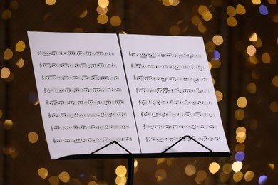 Photo of Note stand with music sheets against blurred lights, closeup. Bokeh effect