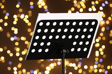 Photo of Note stand with music sheets against blurred lights, closeup. Bokeh effect