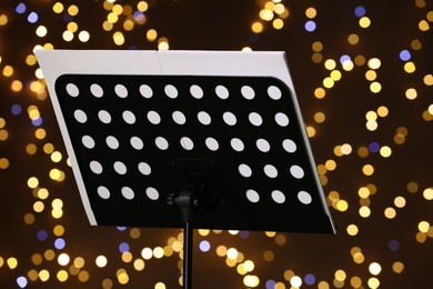 Photo of Note stand with music sheets against blurred lights, closeup. Bokeh effect
