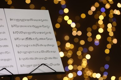 Photo of Note stand with music sheets against blurred lights, closeup. Space for text