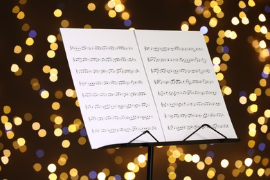 Photo of Note stand with music sheets against blurred lights, closeup. Bokeh effect