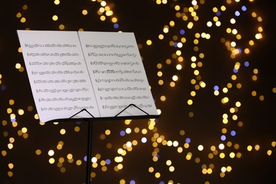 Photo of Note stand with music sheets against blurred lights, closeup. Space for text