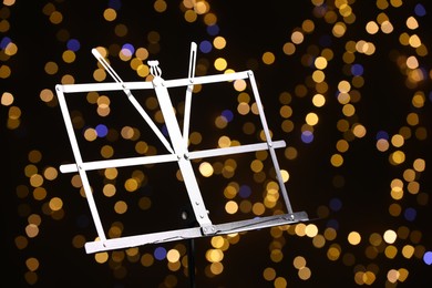 Photo of One empty note stand against blurred lights, closeup. Bokeh effect