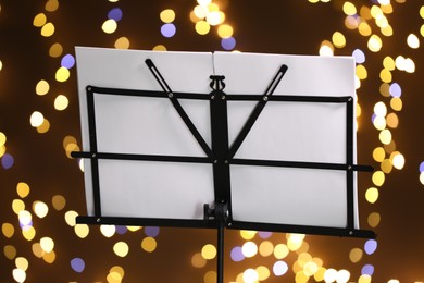 Photo of Note stand with music sheets against blurred lights, closeup. Bokeh effect