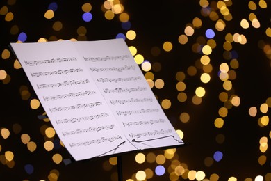 Photo of Note stand with music sheets against blurred lights, closeup. Bokeh effect