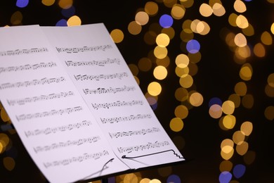Photo of Note stand with music sheets against blurred lights, closeup. Space for text