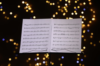 Photo of Note stand with music sheets against blurred lights, closeup. Bokeh effect