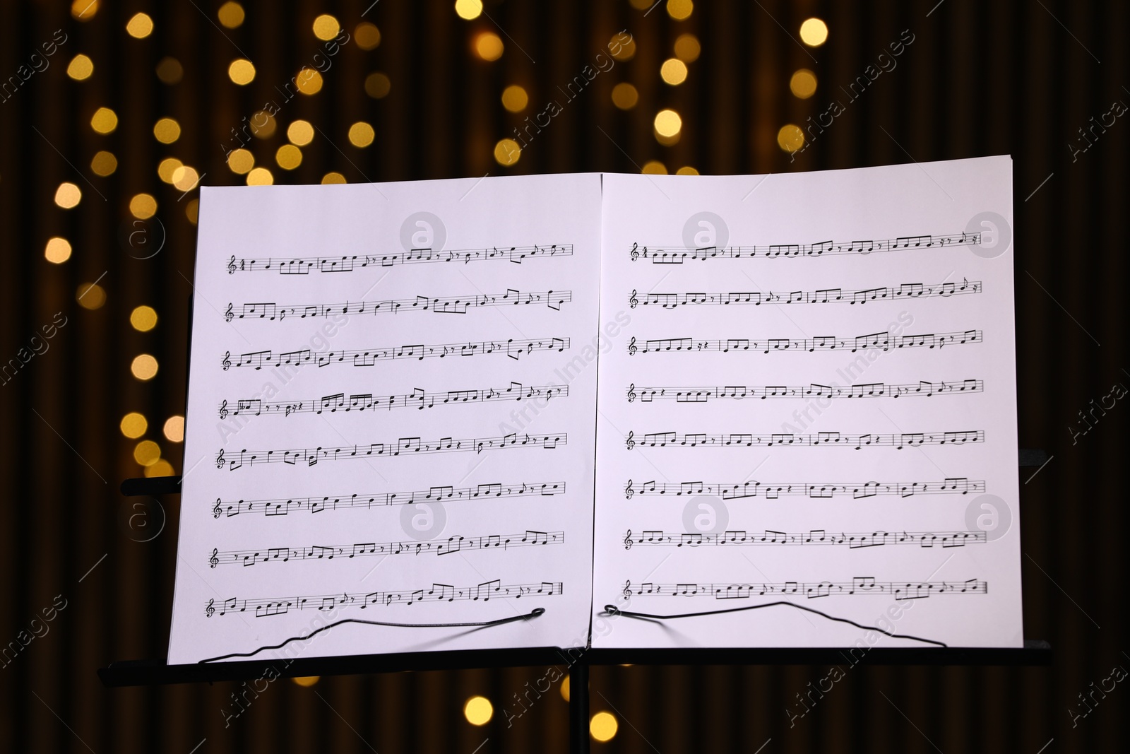 Photo of Note stand with music sheets against blurred lights, closeup. Bokeh effect
