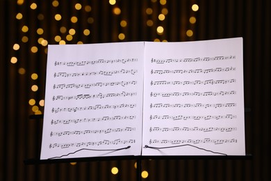 Photo of Note stand with music sheets against blurred lights, closeup. Bokeh effect