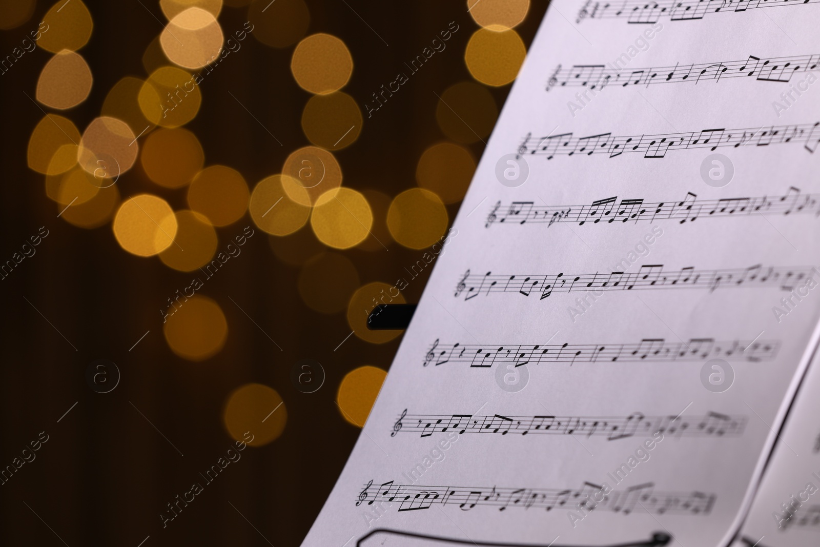 Photo of Music sheets on stand against blurred lights, closeup. Space for text