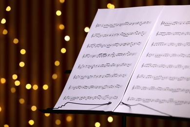 Photo of Note stand with music sheets against blurred lights, closeup. Space for text