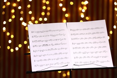 Photo of Note stand with music sheets against blurred lights, closeup. Bokeh effect