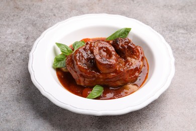 Photo of Traditional ossobuco dish with beef steak, sauce and basil on grey table, closeup