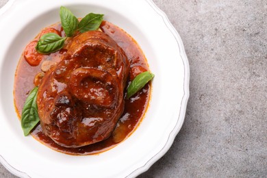 Photo of Traditional ossobuco dish with beef steak and sauce on grey table, top view. Space for text