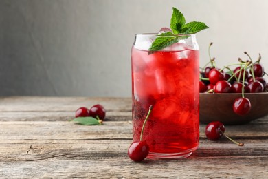 Photo of Tasty cherry soda with ice cubes, berries and mint on wooden table, closeup. Space for text