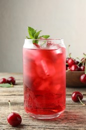 Photo of Tasty cherry soda with ice cubes, berries and mint on wooden table, closeup