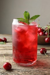 Photo of Tasty cherry soda with ice cubes, berries and mint on wooden table, closeup