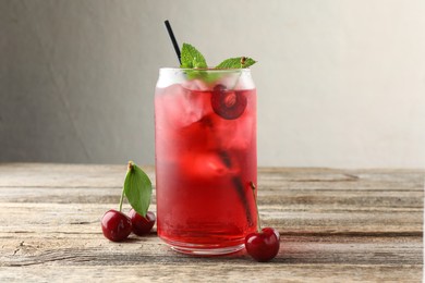 Photo of Tasty cherry soda with ice cubes, berries and mint on wooden table, closeup