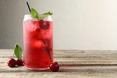 Photo of Tasty cherry soda with ice cubes, berries and mint on wooden table, closeup. Space for text