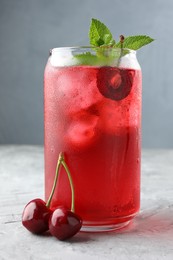 Photo of Tasty cherry soda with ice cubes, berries and mint on grey textured table, closeup