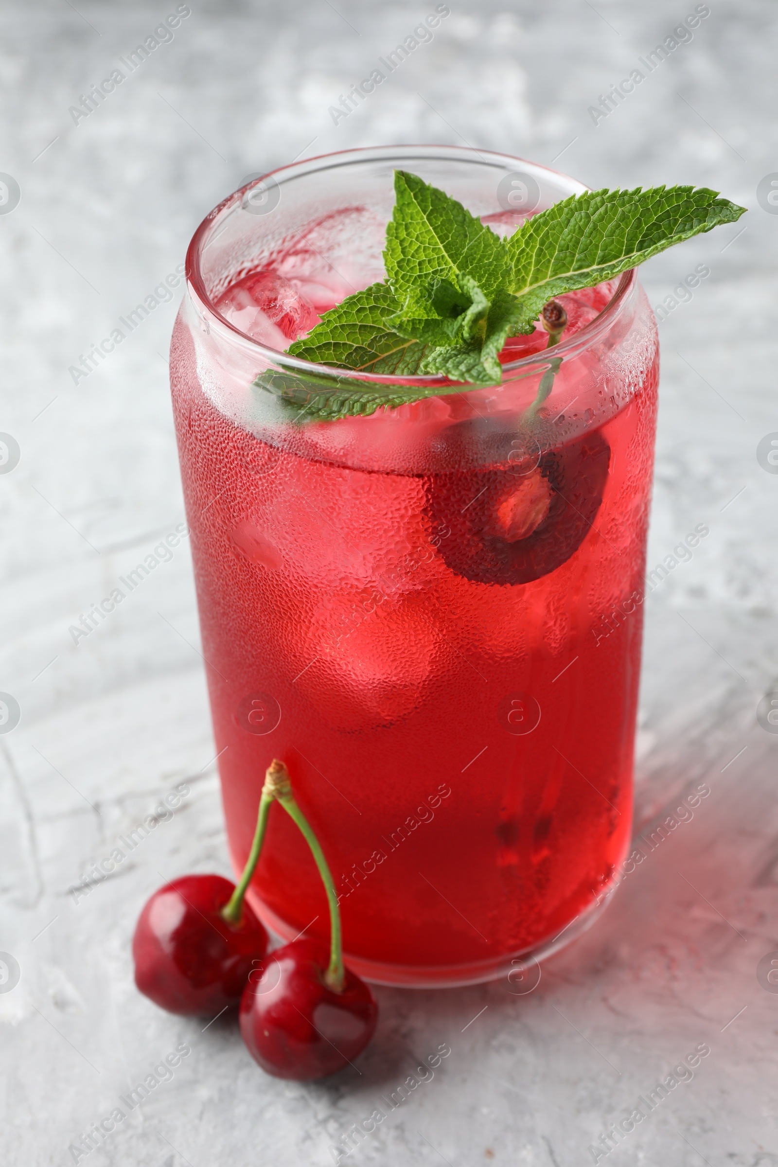 Tasty cherry soda with ice cubes, berries and mint on grey textured table, closeup Photo of Tasty cherry soda with ice cubes, berries and mint on grey textured table, closeup