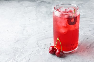 Photo of Tasty cherry soda with ice cubes and berries on grey textured table, closeup. Space for text