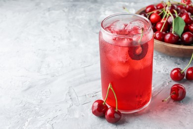 Photo of Tasty cherry soda with ice cubes and berries on grey textured table, closeup. Space for text