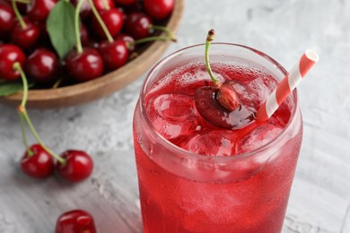 Photo of Tasty cherry soda with ice cubes and berries on grey textured table, closeup