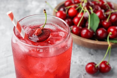 Photo of Tasty cherry soda with ice cubes and berries on grey textured table, closeup