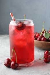 Photo of Tasty cherry soda with ice cubes and berries on grey textured table, closeup