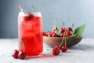 Photo of Tasty cherry soda with ice cubes and berries on grey textured table, closeup