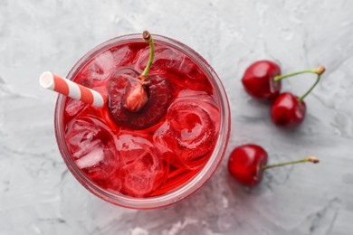 Photo of Tasty cherry soda with ice cubes and berries on grey textured table, flat lay