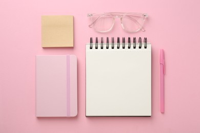 Photo of Notebooks, sticky notes, glasses and pen on pink background, flat lay