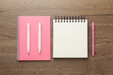 Photo of Notebooks and pens on wooden table, flat lay