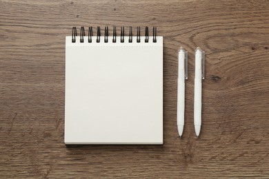 Photo of Notebook and pens on wooden table, flat lay