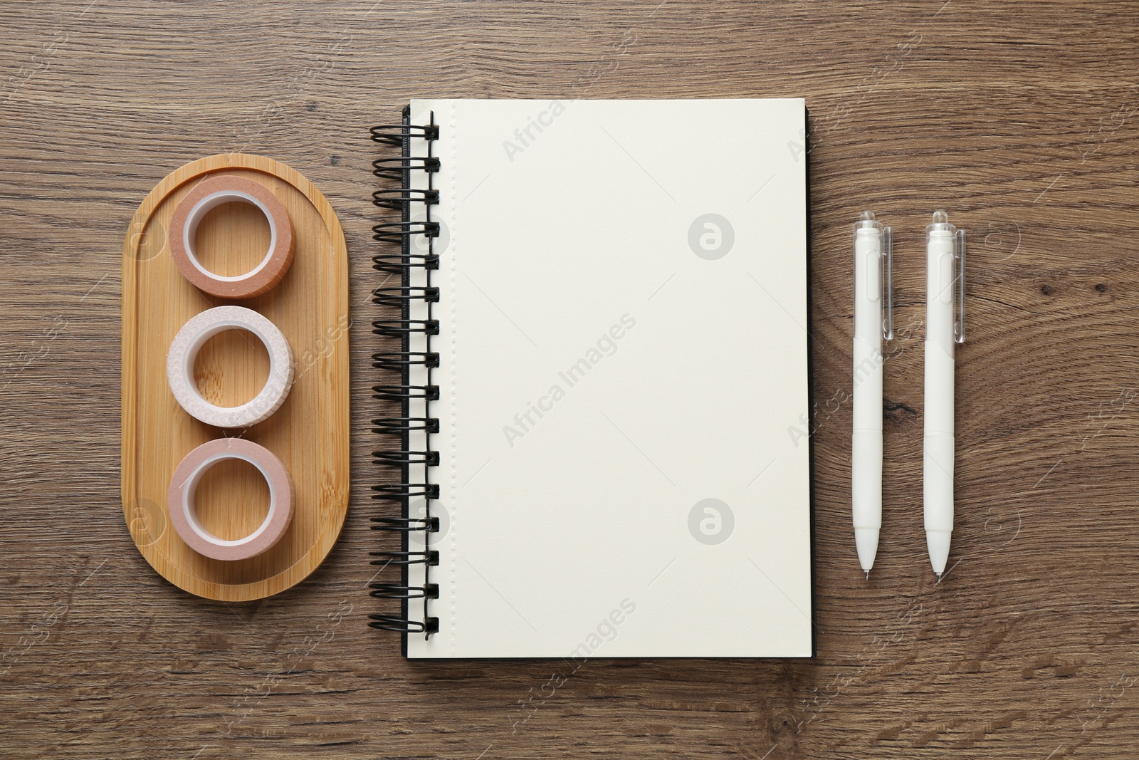 Photo of Notebook, decorative craft tapes and pens on wooden table, flat lay