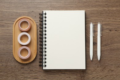 Photo of Notebook, decorative craft tapes and pens on wooden table, flat lay