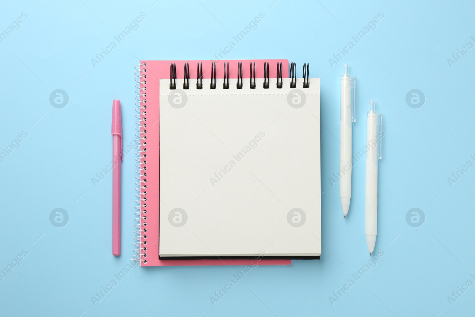 Photo of Notebooks and pens a on light blue background, flat lay