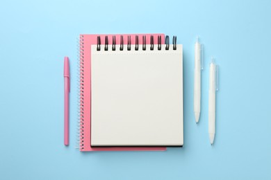 Photo of Notebooks and pens a on light blue background, flat lay