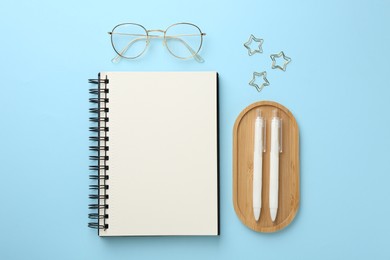 Photo of Notebook, glasses, pens and paper clips on light blue background, flat lay