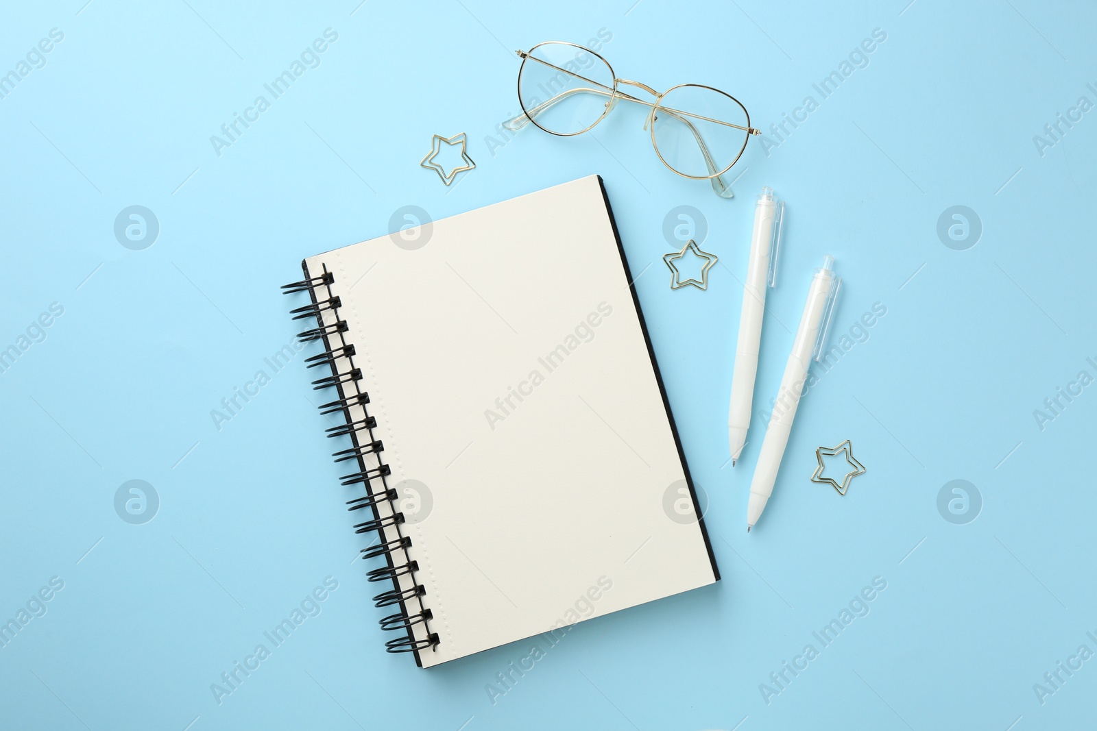 Notebook, glasses, pens and paper clips on light blue background, flat lay Photo of Notebook, glasses, pens and paper clips on light blue background, flat lay