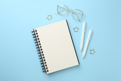 Photo of Notebook, glasses, pens and paper clips on light blue background, flat lay