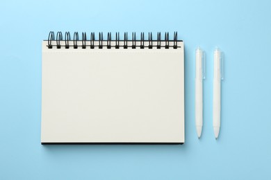 Photo of Notebook and pens a on light blue background, flat lay