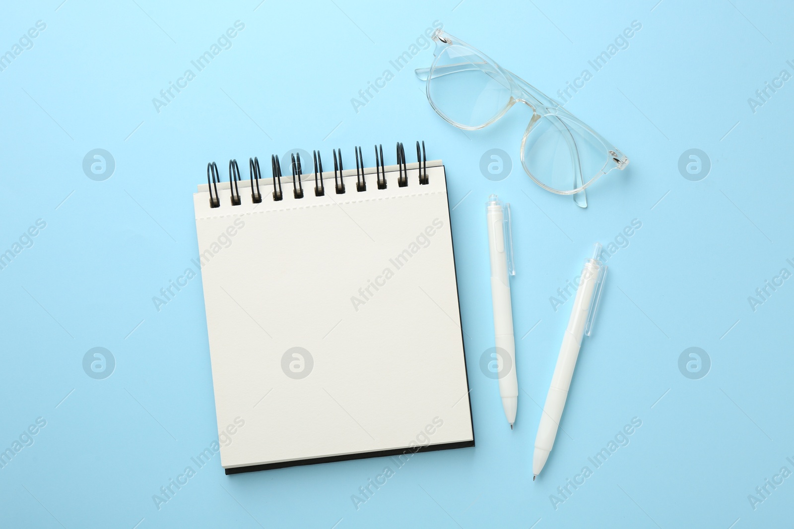 Photo of Notebook, glasses and pens a on light blue background, flat lay