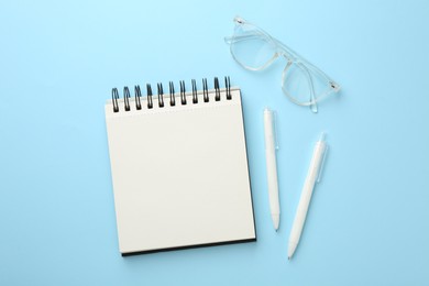 Photo of Notebook, glasses and pens a on light blue background, flat lay