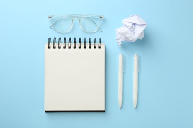 Photo of Notebook, glasses, crumpled paper and pens a on light blue background, flat lay