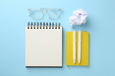 Photo of Notebooks, glasses, crumpled paper and pens a on light blue background, flat lay