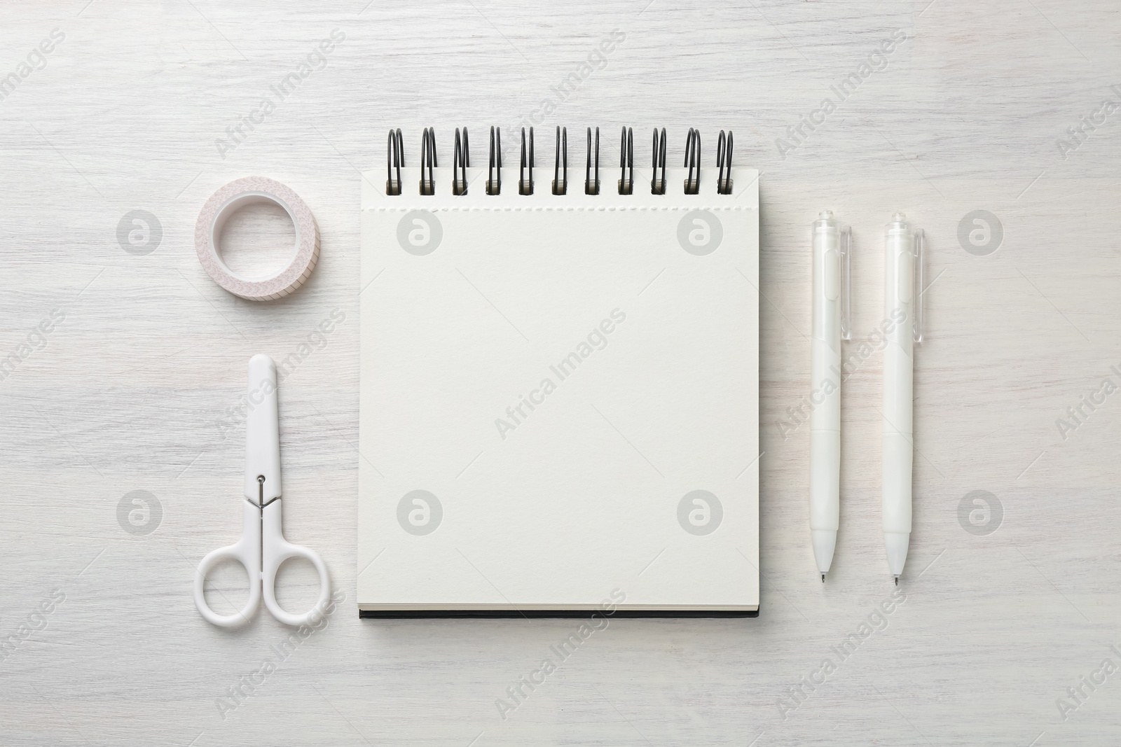 Notebook, pens, scissors and decorative craft tape on light wooden table, flat lay Photo of Notebook, pens, scissors and decorative craft tape on light wooden table, flat lay