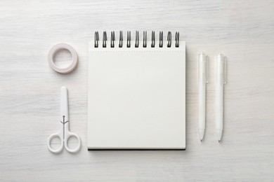 Photo of Notebook, pens, scissors and decorative craft tape on light wooden table, flat lay
